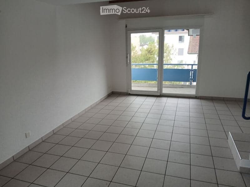 Empty room with tiled floor, white walls, and large sliding glass door leading to a balcony.