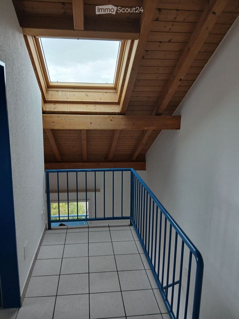 Staircase with wooden ceiling beams and skylight, blue railing, tiled floor, and view of outdoor area below.