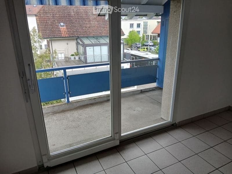 Balcony with a blue railing, tiled floor, and a view of neighboring buildings and a street.