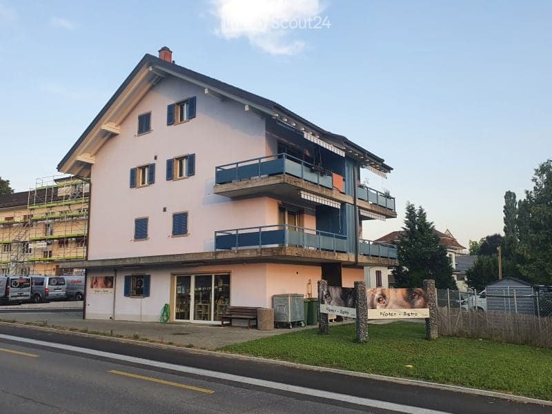 Two-story building with light pink facade, multiple windows, and balconies on the upper floor.