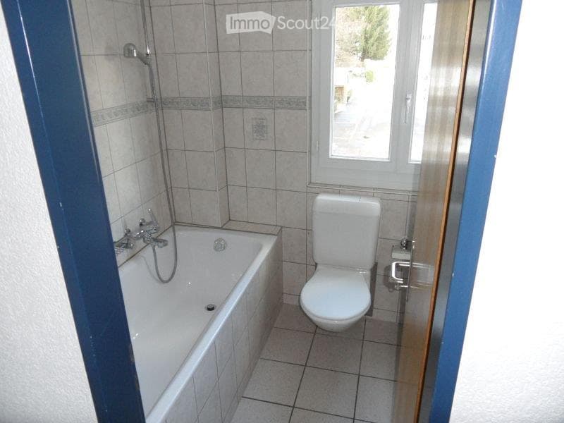 Bathroom with a white bathtub, toilet, tiled walls, and a window offering a view of the outside.