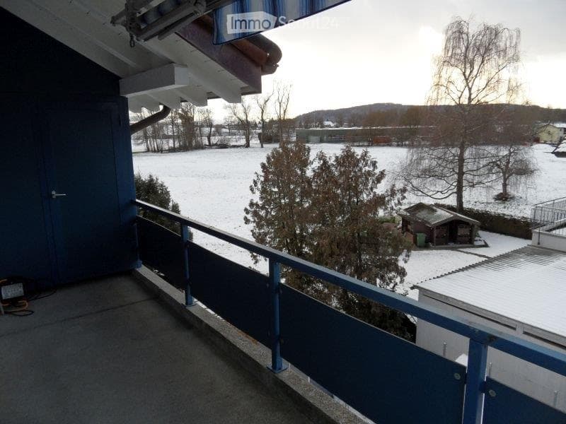 Balcony overlooking a snowy landscape with trees and a small shed in the distance.