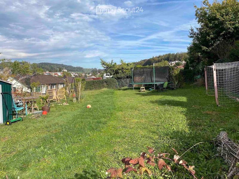 A well-maintained garden with a trampoline, outdoor furniture, and a view of the surrounding neighborhood.