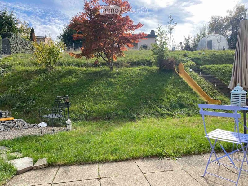 Garden with a raised lawn, patio seating area, and scenic hillside view.