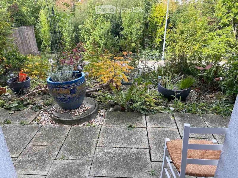 Garden area with potted plants, stone pathway, and a single white chair with woven seat.