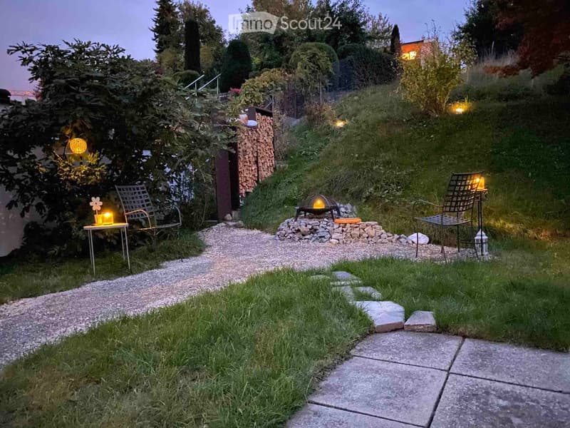 Well-maintained garden with a fire pit, seating area, small tables, and decorative lighting.