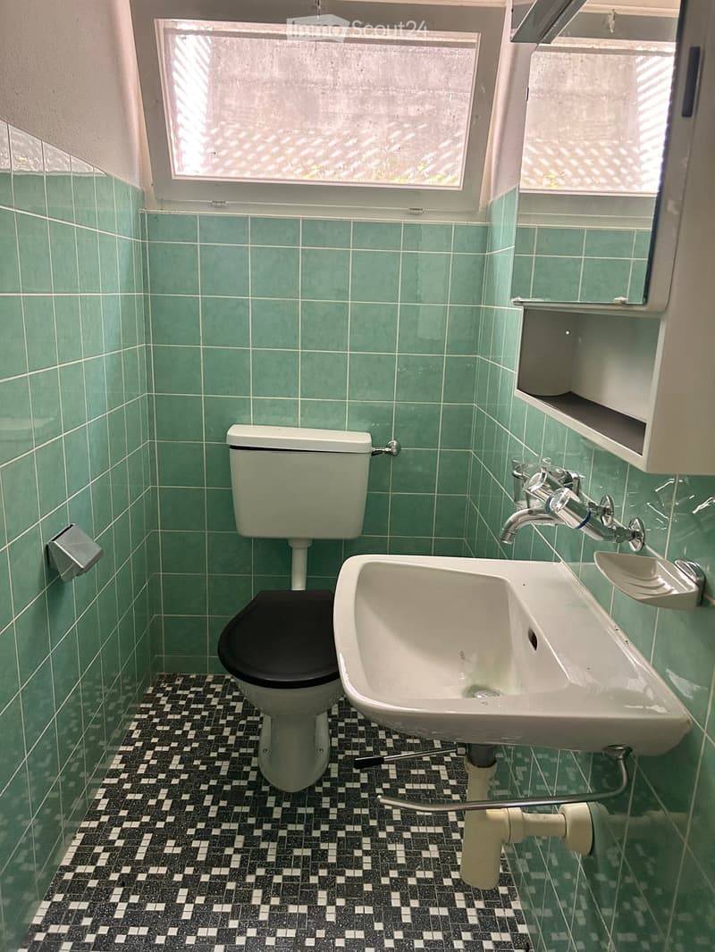 Bathroom with green tiled walls, black and white checkered floor, toilet, sink, faucet, mirror, and cabinet.