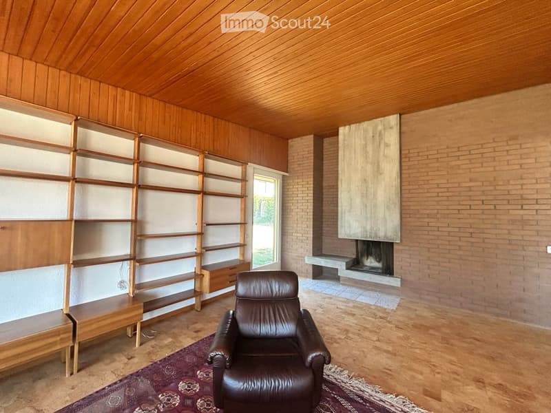 Living room with wooden walls and ceiling, leather armchair, built-in bookshelf, brick fireplace, and bench.