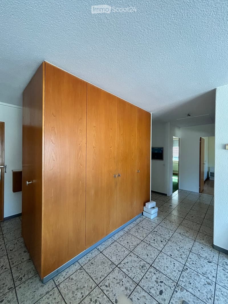 Empty hallway with tiled floor, light-colored walls, and a large wooden wardrobe on the left side.