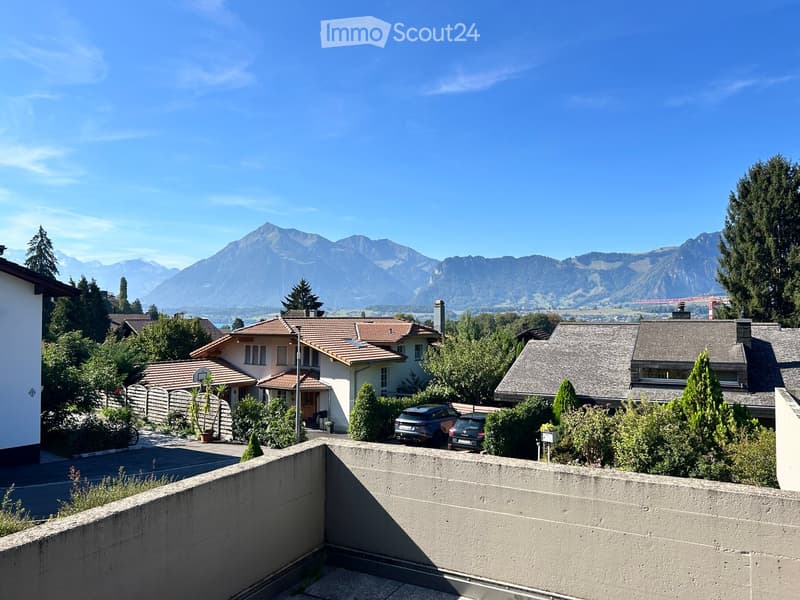Residential area with houses, trees, parked cars, and a scenic mountain view in the background.