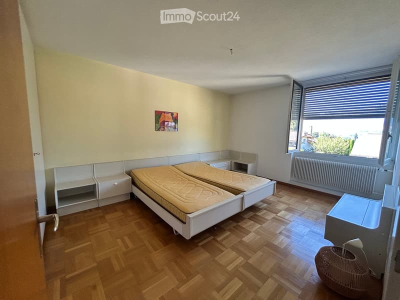A small bedroom with two single beds, built-in storage, a nightstand, a radiator, and a wicker basket near the door.