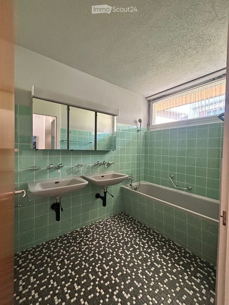 Bathroom with green tiled walls, two sinks, a bathtub, and a mirrored cabinet above the sinks.