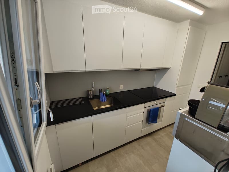 Modern kitchen with white cabinets, black countertop, stainless steel sink, oven, and coffee machine.