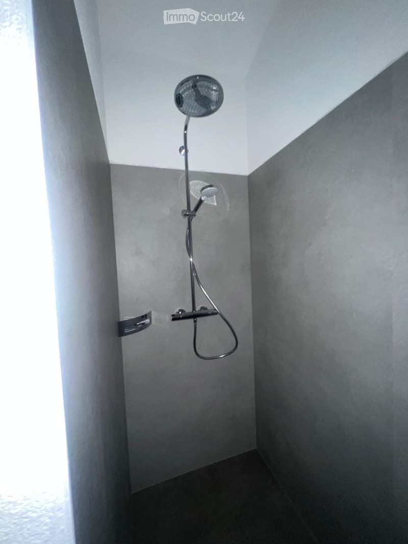 Shower with dual shower heads, gray tiled walls, black floor tiles