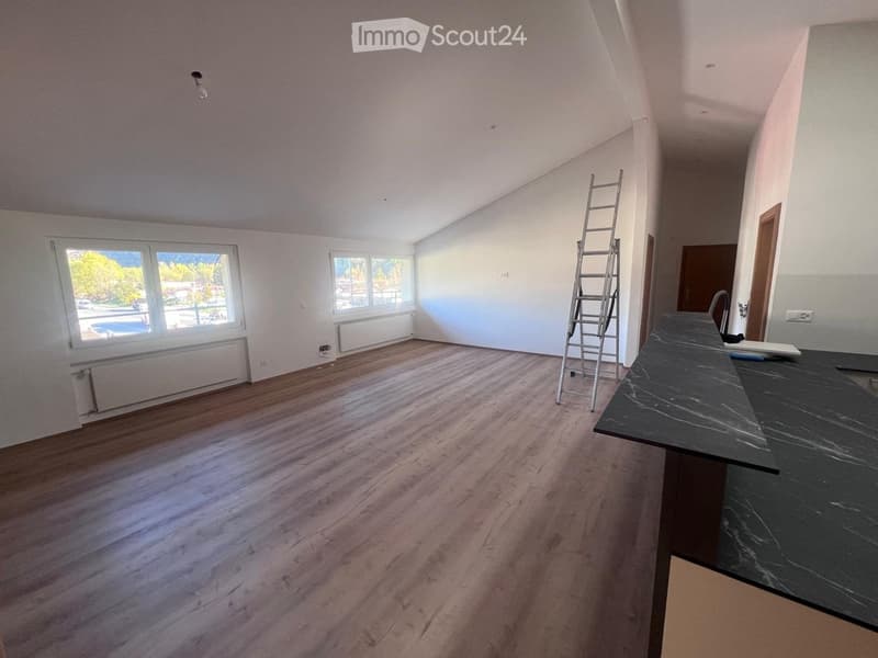 Spacious living room with large windows, hardwood-style flooring, and a ladder leaning against the wall, indicating ongoing renovation or construction work.