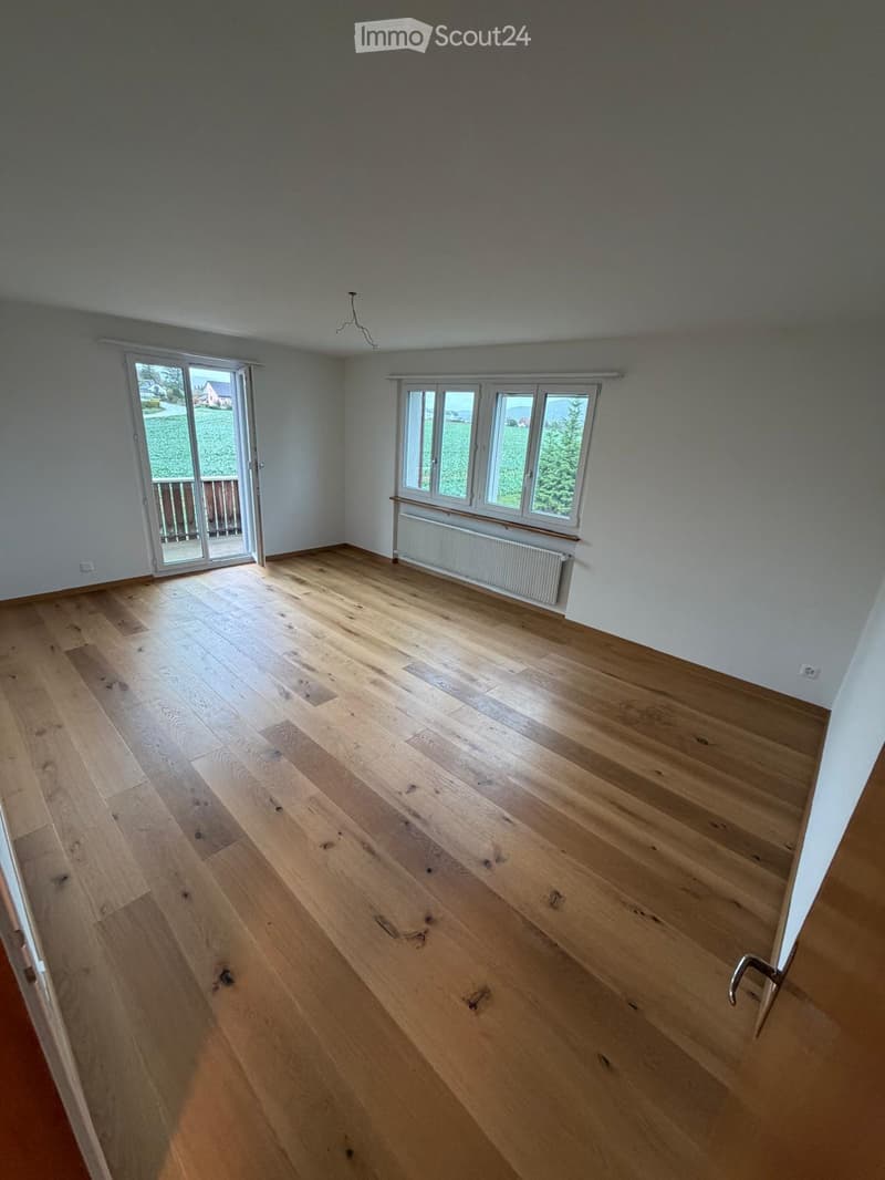 Empty room with wooden flooring, large windows, and a sliding glass door leading to a balcony.