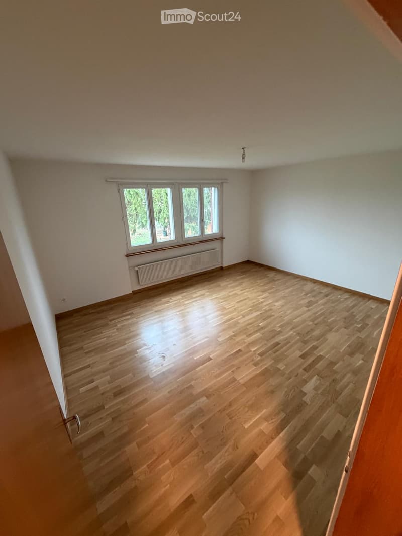 Empty room with wooden flooring, white walls, and large windows with a radiator below them.