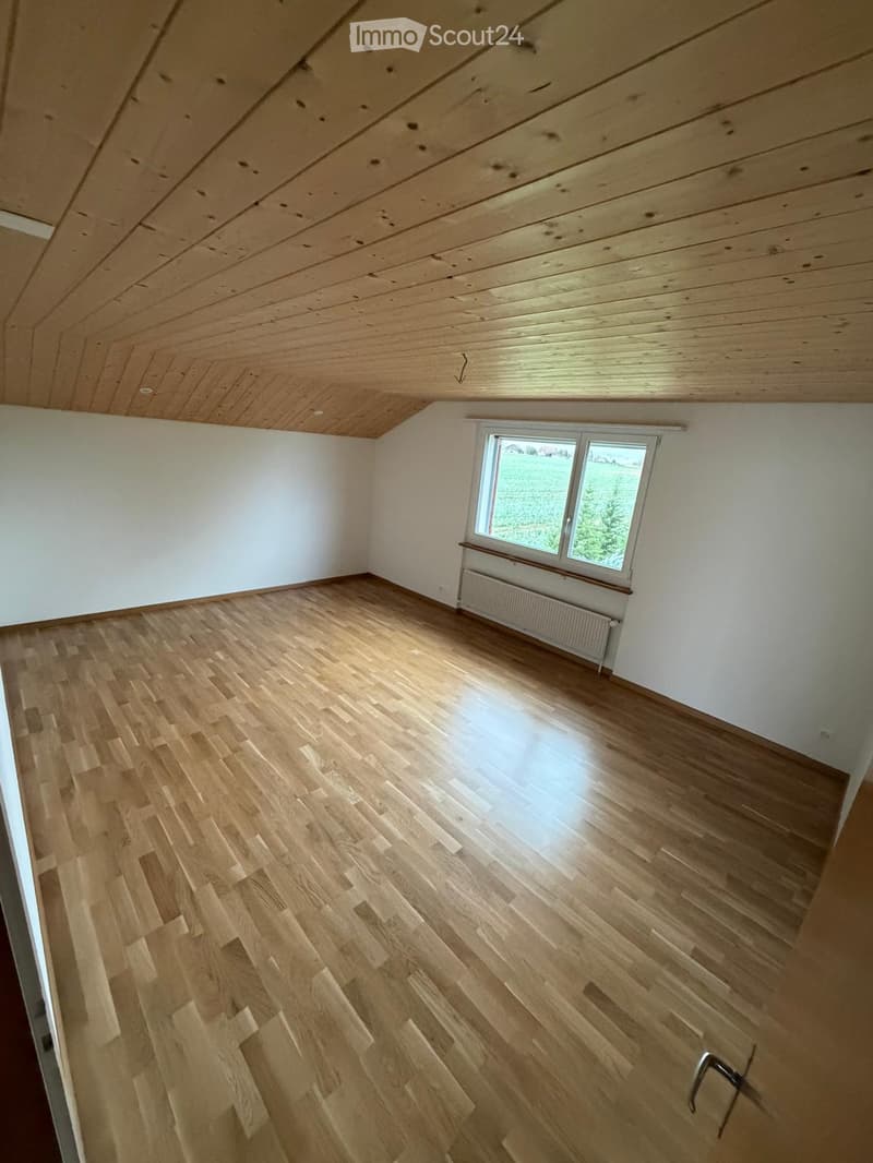 Empty room with wooden flooring, white walls, and a large window with a radiator below it.