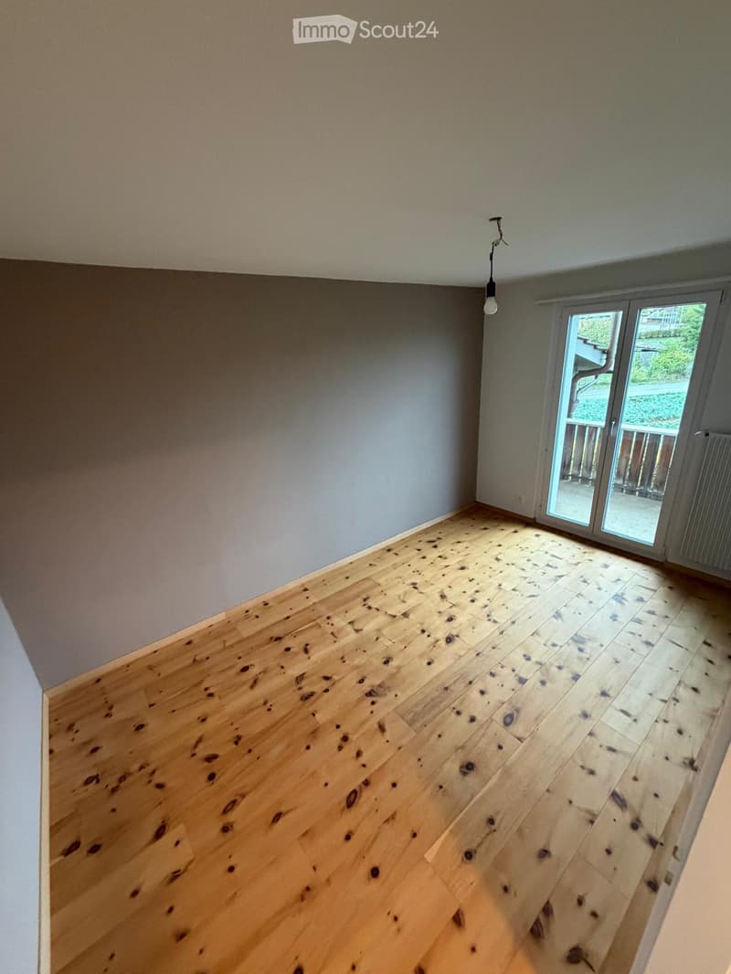 Empty room with wooden flooring and large sliding glass door leading to a balcony.