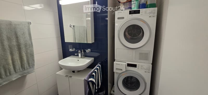 Bathroom with a white sink, mirror, towel, and a stacked washing machine and dryer unit.