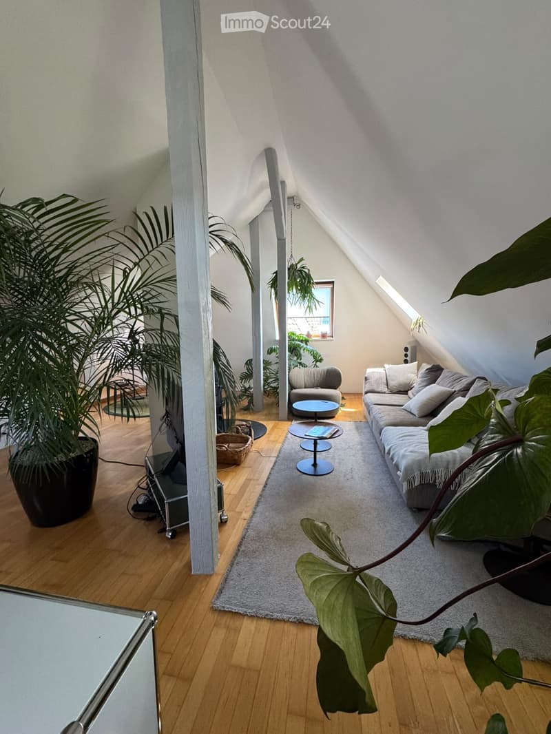 Modern living room with wooden flooring, large window, grey sofa, armchair, coffee table, and plants.