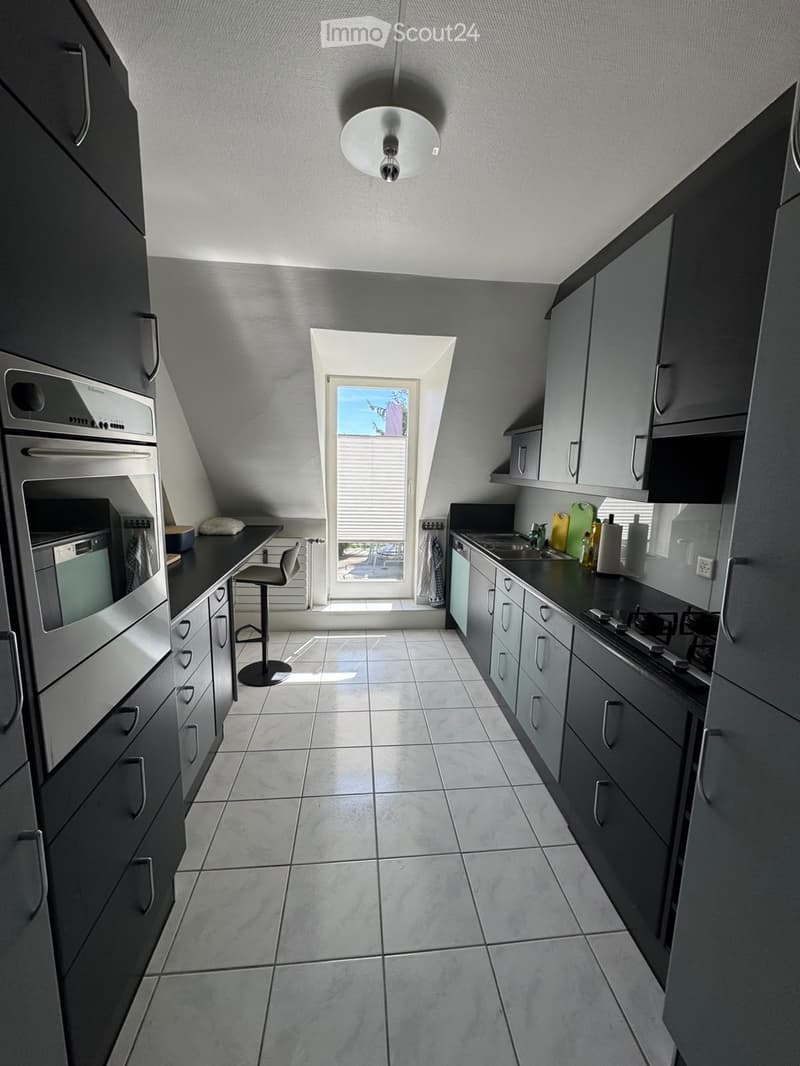 Modern kitchen with grey cabinets, stainless steel appliances, tiled floor, and a small window with blinds.