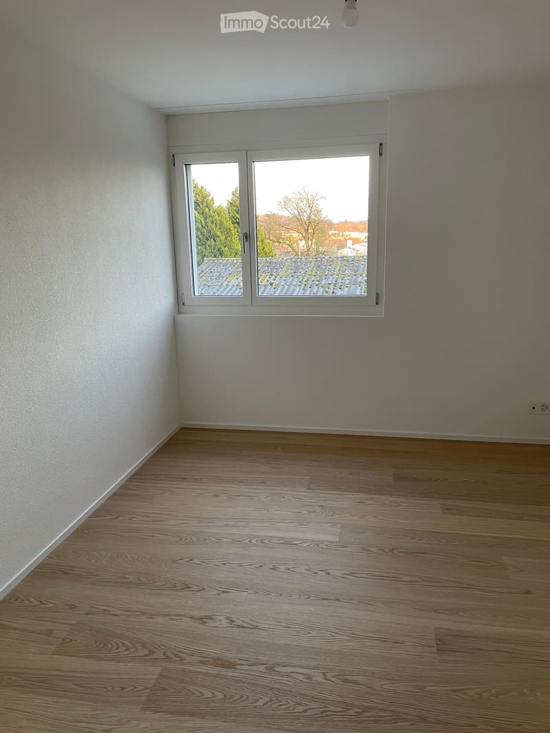 Empty room with wooden flooring, white walls, and a large window offering a view of the outside.