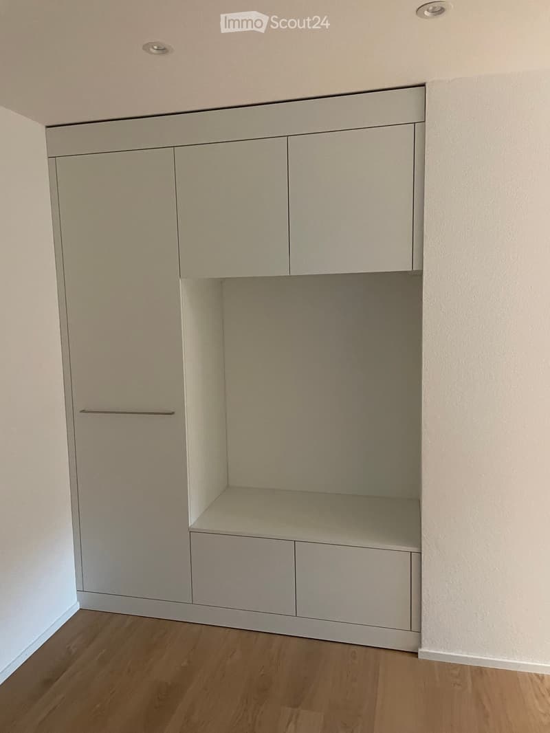 Empty built-in closet with light-colored wood cabinets and drawers, featuring a single shelf and a small open compartment.