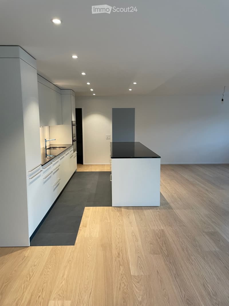 Empty kitchen with white cabinets, a central island, and wooden flooring.