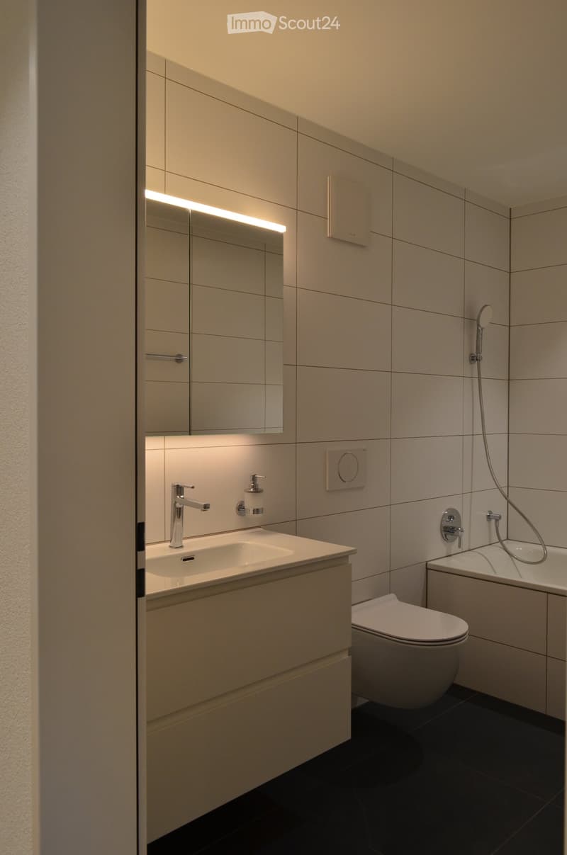 Modern bathroom with a white sink, chrome faucet, large mirror with built-in lighting, toilet, bathtub, and showerhead.