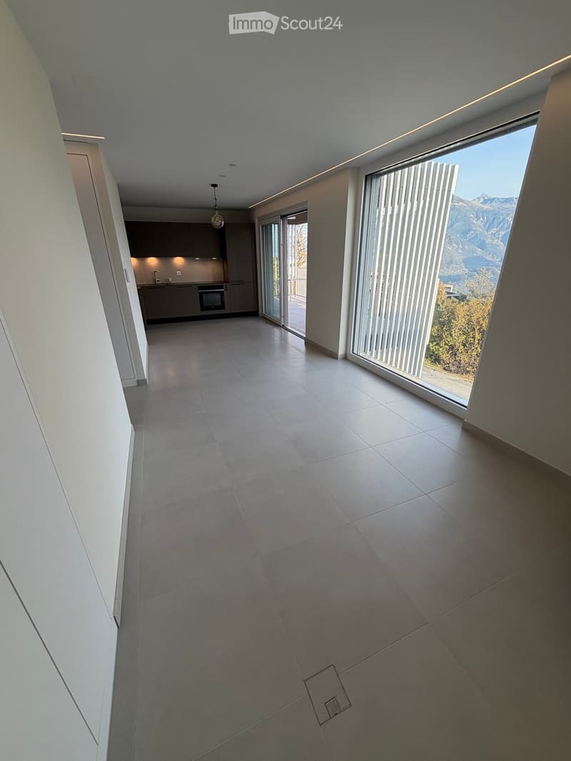 Modern hallway with large windows and a view of mountains, leading to a kitchen area with cabinets and appliances.