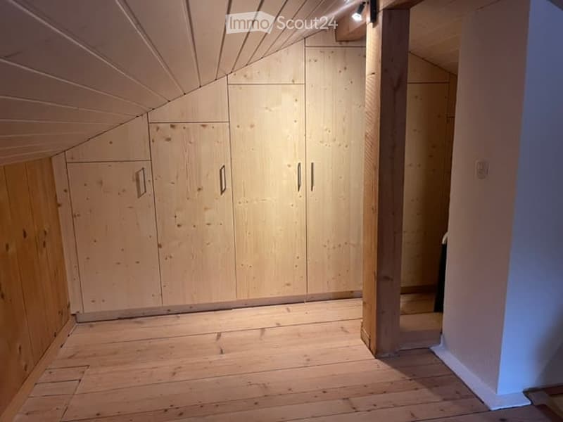 Empty room with wooden floor and built-in wooden wardrobes, featuring a slanted ceiling and recessed lighting.