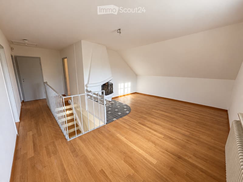Empty room with wooden flooring, white walls, a staircase with white railings, and a small rug near the fireplace.
