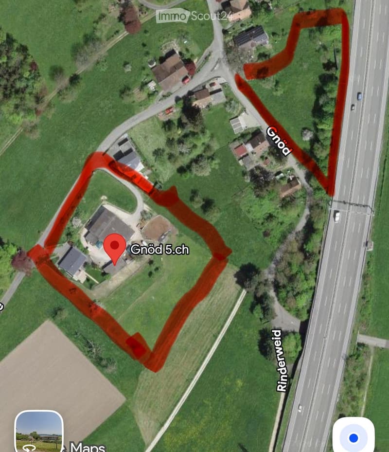 Aerial view of a residential property with multiple buildings, surrounded by green fields and a nearby highway.