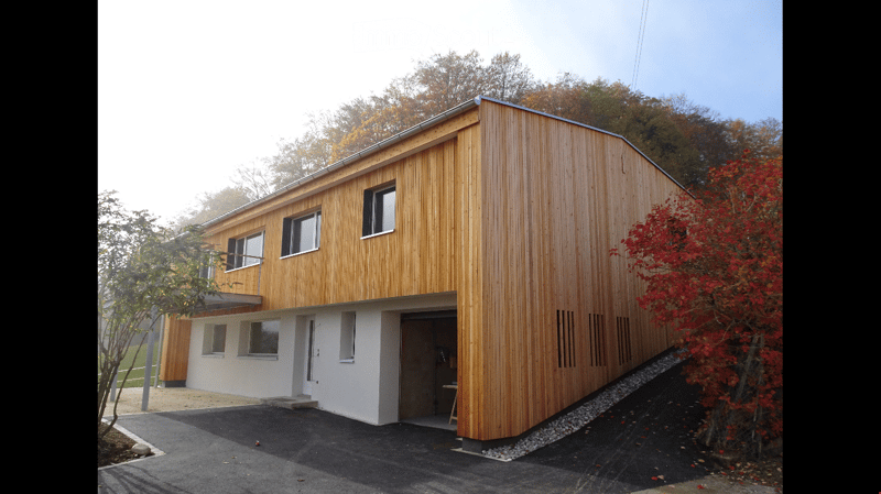 Modern two-story house with wooden siding, raised ground floor, garage, and multiple windows.