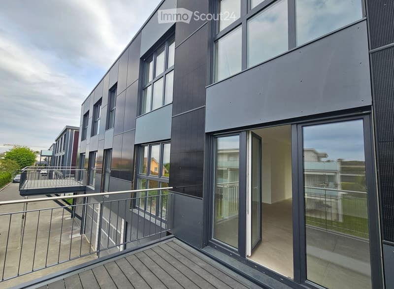 Modern multi-story building with large windows and balconies, featuring a sleek, contemporary design with grey and black panels.