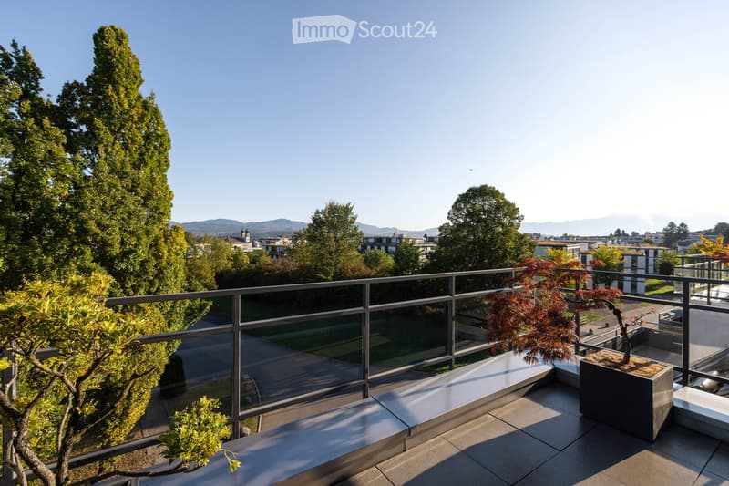 Modern balcony with glass railing, potted plants, and scenic city view with trees and mountains.
