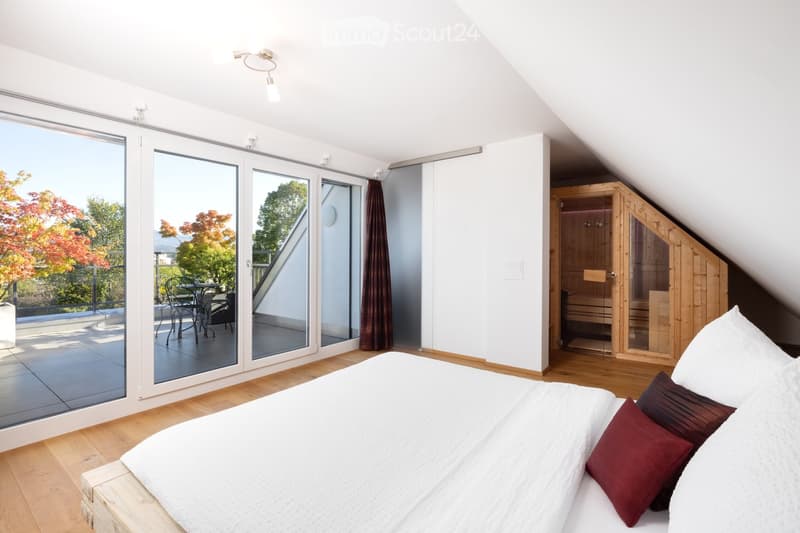 Bright bedroom with a large bed, wooden sauna, and a balcony with outdoor furniture.