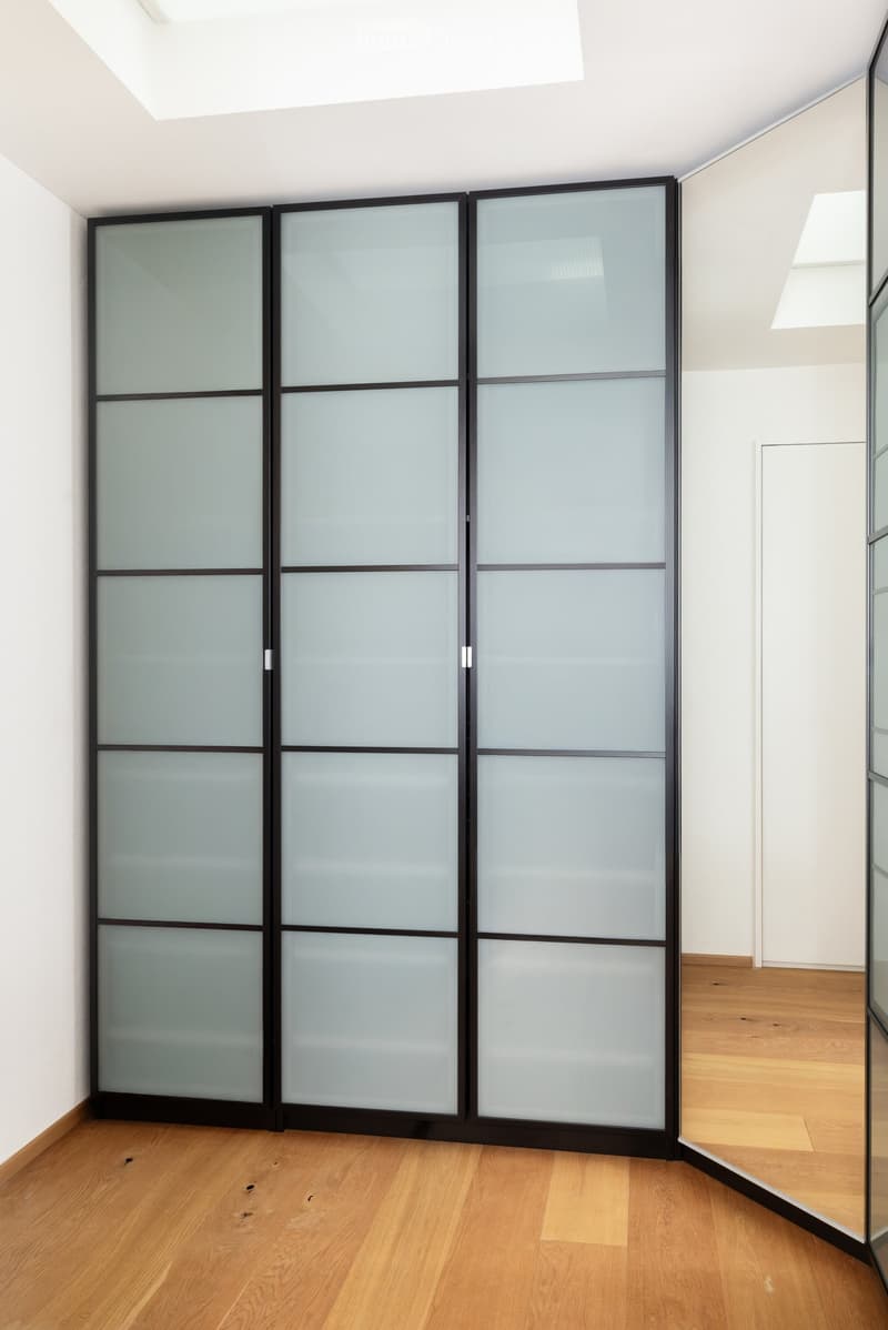 Empty room with light wooden flooring and white walls, featuring a large sliding glass partition with a black frame.