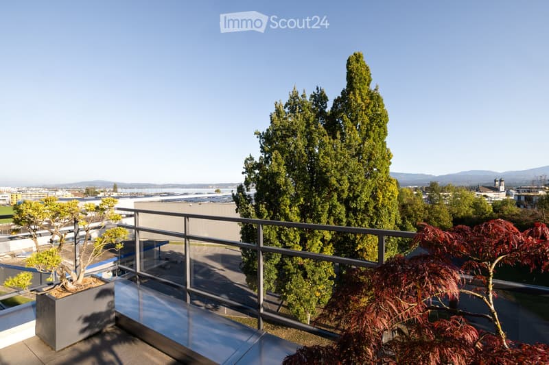 Balcony with a modern metal railing, overlooking a cityscape with trees and distant mountains.
