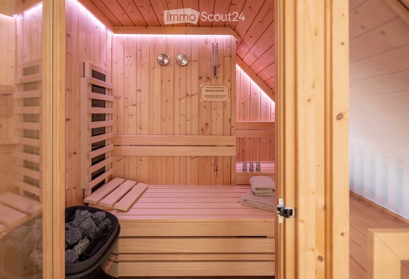 A wooden sauna with a wooden bench, wooden slats, a wooden door, wooden walls, a wooden ceiling, a thermostat, a wooden sign, towels, essential oils, and stone rocks.
