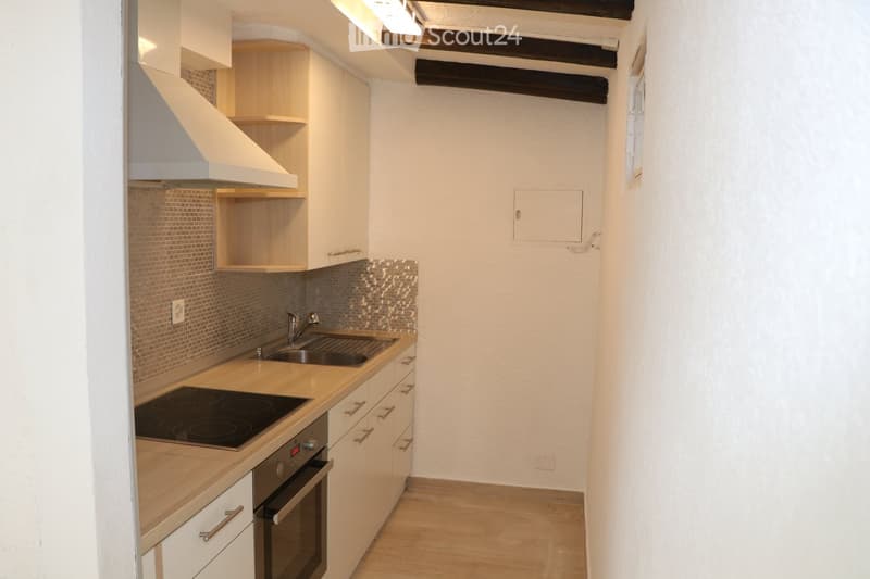 Modern kitchen with white cabinets, wooden countertops, stainless steel sink, induction cooktop, and built-in oven. Exposed wooden beams on the ceiling.