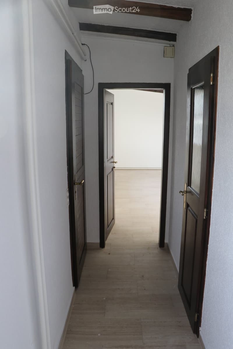 Empty hallway with wooden flooring, white walls, and several doors on both sides.