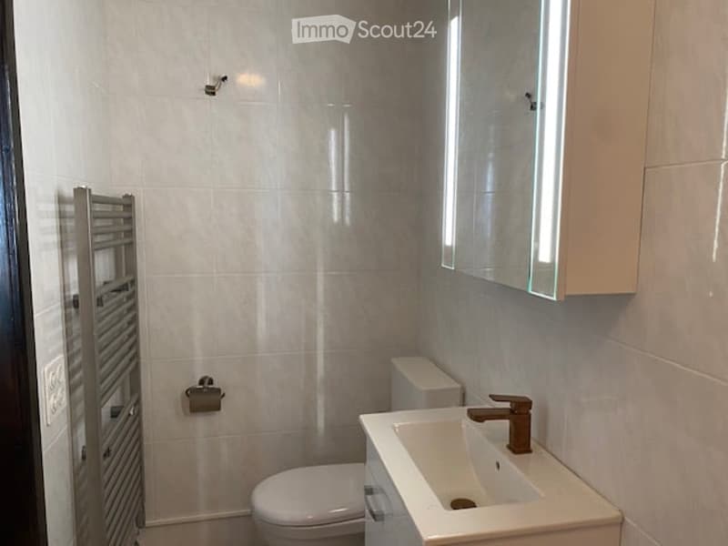 Modern bathroom with white tiles, a toilet, a sink with a modern faucet, a mirror cabinet, and a towel radiator.