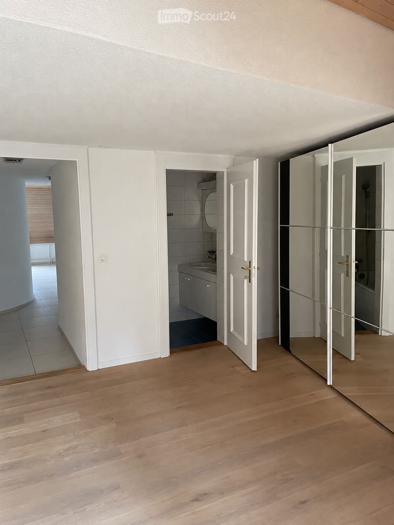 Empty hallway with wooden flooring, white walls, and open doors leading to a bathroom and another room.
