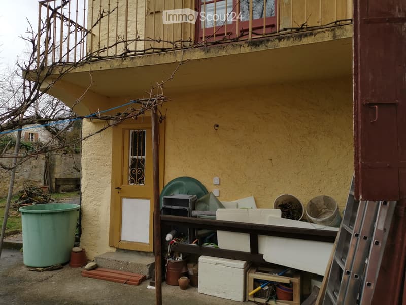 yellow exterior wall, entrance door, balcony with railings, large buckets, boxes, ladder