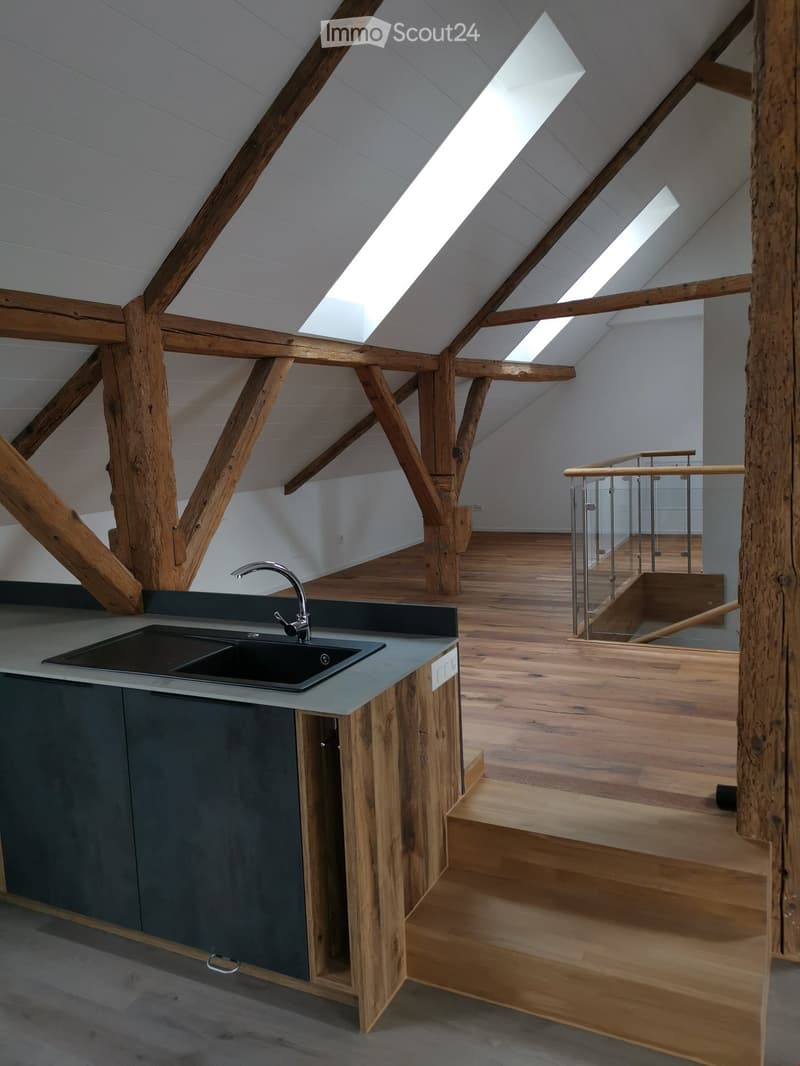 kitchen in an attic room with wooden beams, wooden floor, and a sink with a faucet