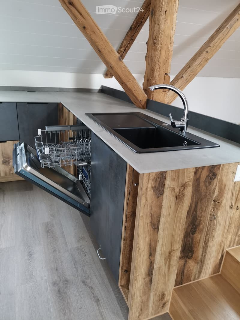 Modern kitchen with wooden walls and countertops, stainless steel sink, open dishwasher, wooden ceiling beams