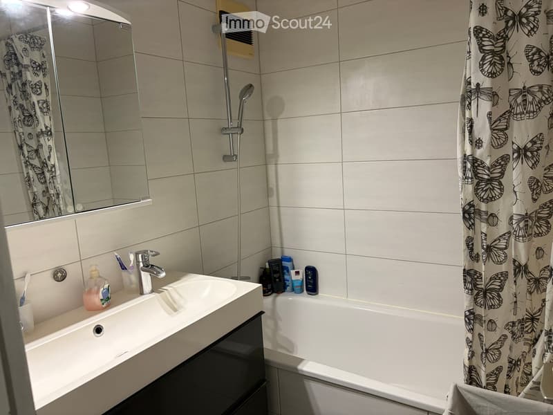 Modern bathroom with a white sink, bathtub, and shower area. The sink has a chrome faucet and toothbrush holder, and the bathtub is covered with a butterfly-patterned shower curtain. A large mirror is mounted above the sink.