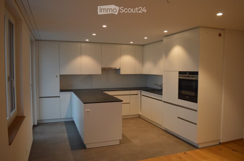 Modern kitchen with white cabinets, black countertop, and built-in oven. Features a sleek design with recessed lighting and a window on the left side.